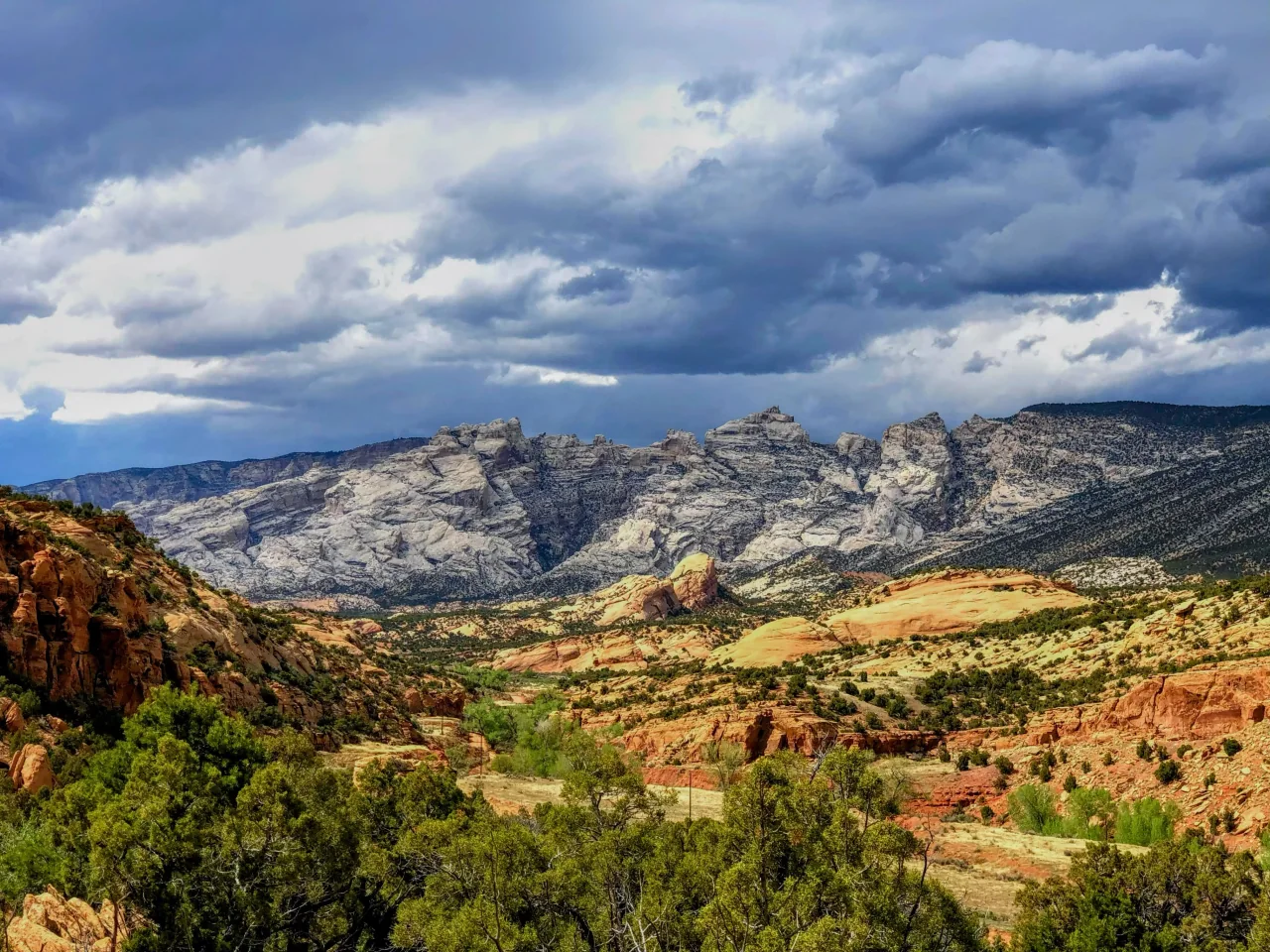 Split Mountain beneath a cloudy sky, with orange sandstone and green shrubs in the foreground